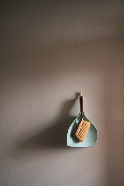 A person wearing a light green cleaning glove is organizing or placing white binders or folders onto a dark wooden shelf in an indoor setting. The shelf contains a collection of hardcover books with g
